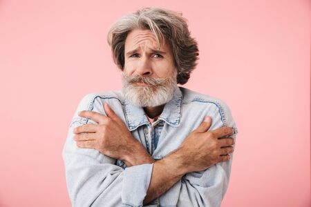 Portrait of an upset middle aged man wearing casual outfit standing isolated over pink background,...