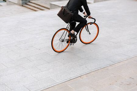 Cropped image of a businessman wearing suit, carrying briefcase outdoors riding on a bicycle