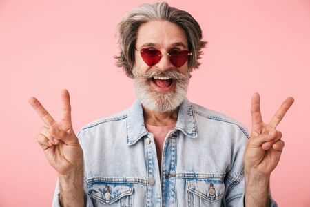 Portrait of happy old man with gray beard wearing fashion sunglasses smiling and showing peace...