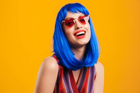 Portrait of funny caucasian woman wearing blue wig and sunglasses looking at camera and laughing...