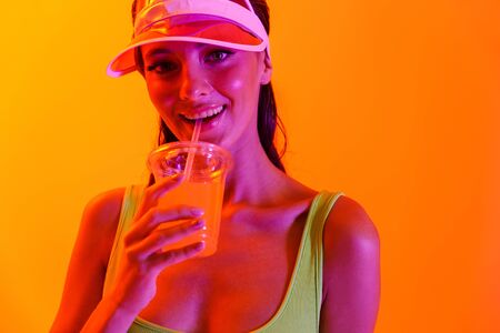 Portrait of a positive young stylish girl in sport lifestyle clothes and transparent cap drinking...
