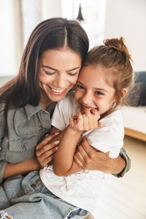 Image of happy family mother and little daughter hugging and smiling while resting at home in...