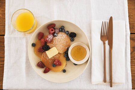 Photo from top of breakfast plate and cutlery. Pancakes with berries, honey, orange juice on kitchen...