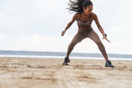 Attractive young african fitness woman exercising at the beachの写真素材