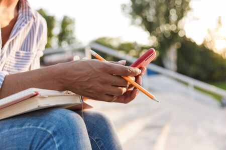 Close up of a young african woman studying while sitting on steps outdoors, using mobile phoneの写真素材