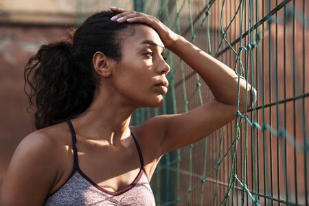 Close up of a beautiful young african fitness woman leaning on a fence outdoorsの写真素材