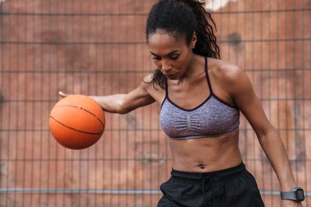 Attractive young african sportswoman playing basketball at the playground outdoorsの写真素材