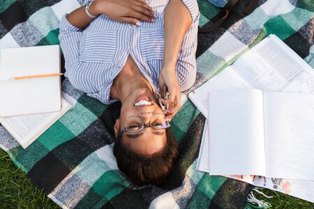 Top view of an attractive young african woman wearing casual outfit laying on a blanket at the park,...