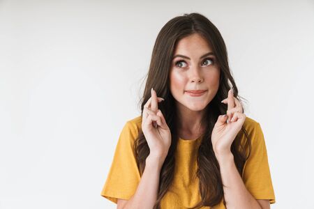 Image of concentrated brunette woman wearing casual t-shirt keeping fingers crossed and wishing good...