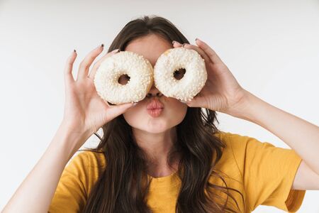 Photo of young woman 20s wearing casual clothes smiling and holding two sweet donuts isolated over white backgroundの写真素材