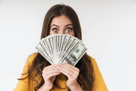 Photo of a surprised excited young girl isolated over white wall background holding money covering...