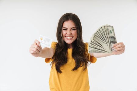 Image of a happy cheery positive young girl isolated over white wall background holding money and credit card.の写真素材