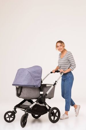 Image of a beautiful positive optimistic young blonde woman mother walking with baby in pram isolated over white background wall.の写真素材