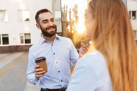 Photo of a young cheery positive man and woman businesspeople outside at the street near business center talking with each other.の写真素材