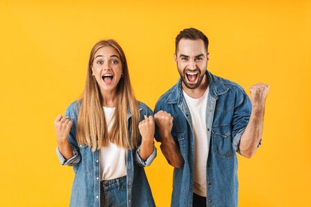 Portrait of an attractive cheerful young couple wearing casual clothing standing isolated over yellow background, celebrating successの写真素材