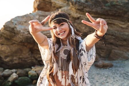 Image of young hippy girl wearing feather headband laughing and showing peace sign while walking by...