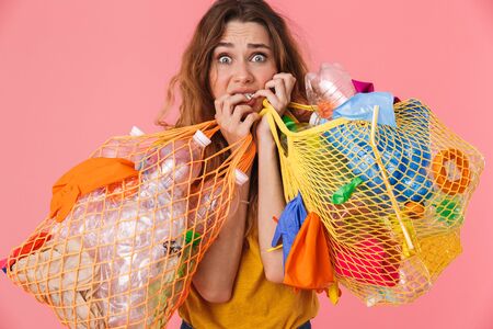 Photo of unhappy scared woman in basic t-shirt holding bags with plastic waste and looking at camera...