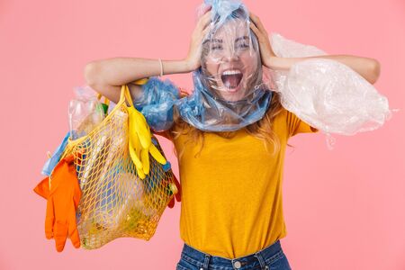 Photo of young nervous woman with pack on her head holding bag with plastic waste isolated over pink...