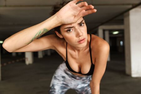 Image of beautiful tied woman in sportswear resting while working out on parkingの写真素材