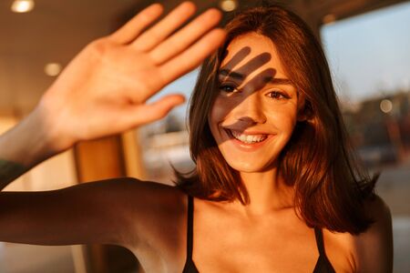 Image of joyful young woman in sportswear covering her face with hand from sunshine while walking on streetの写真素材