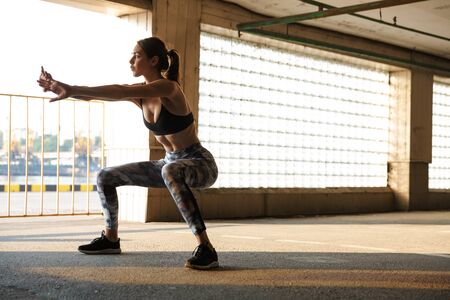 Image of strong attractive woman in sportswear doing exercise while working out on parking near seaportの写真素材
