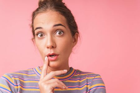 Image closeup of surprised beautiful woman expressing wonder with big eyes while looking at camera isolated over pink backgroundの写真素材