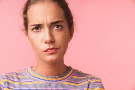 Image closeup of puzzled beautiful woman dressed in colorful clothes frowning and looking at camera isolated over pink backgroundの写真素材