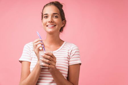 Image closeup of optimistic gorgeous woman smiling and drinking chocolate milk with straw isolated over pink backgroundの写真素材
