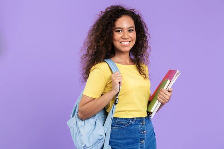 Image of joyful african american student girl with curly hair holding exercise books isolated over...
