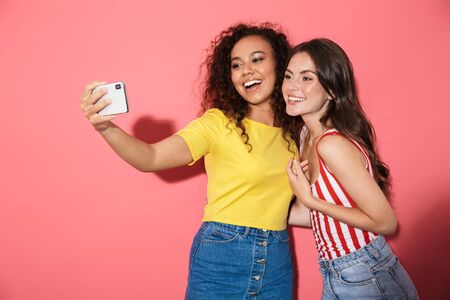 Image of charming multinational girls smiling while taking selfie photo on cellphone isolated over...