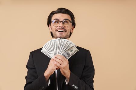 Portrait of a handsome young businessman wearing suit standing isolated over beige background,...