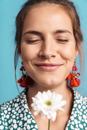 Close up portrait of a lovely young woman wearing shirt and bright earrings standing isolated over...