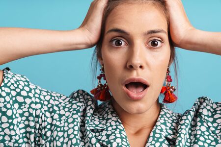 Close up portrait of a lovely excited young woman wearing shirt and bright earrings standing isolated over blue background, looking at cameraの写真素材