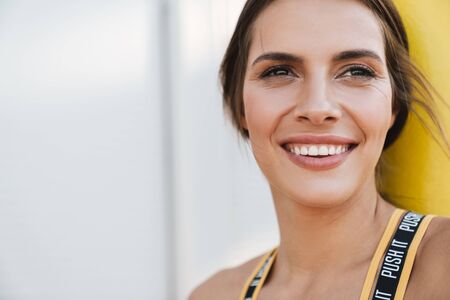 Image closeup of happy woman in sportswear smiling while standing over white wall outdoorsの写真素材