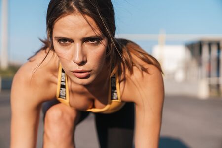 Image closeup of concentrated woman in sportswear getting ready to run while doing workout outdoorsの写真素材