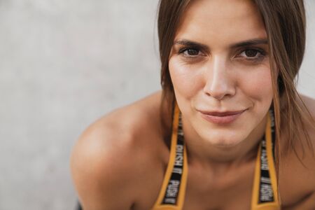 Image closeup of lovely woman in sportswear looking forward while standing over concrete wall outdoorsの写真素材
