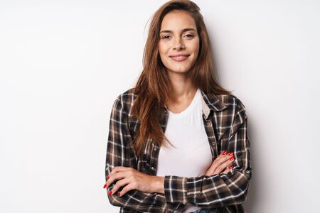 Portrait of a young beautiful girl wearing plaid shirt standing isolated over white background, posing arms foldedの写真素材