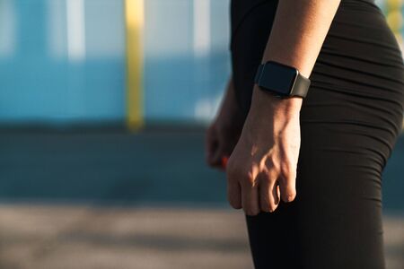 Cropped image closeup of caucasian woman in sportswear standing with wristwatch while doing workout outdoorsの写真素材