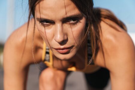 Image closeup of brunette woman in sportswear getting ready to run while doing workout outdoors
