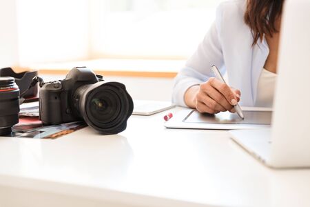 Cropped picture of photographer woman in office sit at the table with camera working by graphic...