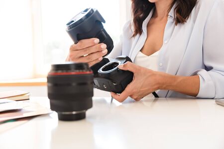 Cropped image of photographer woman in office sit at the table holding camera lenses.の写真素材