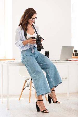 Photo of a cheery positive optimistic young photographer woman in office with camera.の写真素材