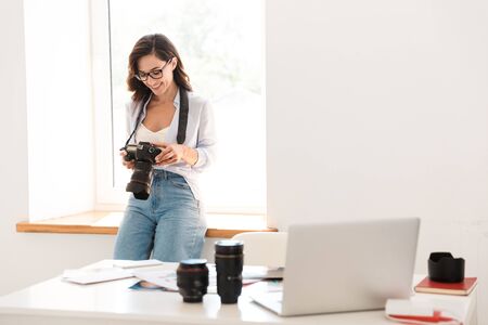 Image of a happy smiling optimistic young photographer woman in office with camera.の写真素材