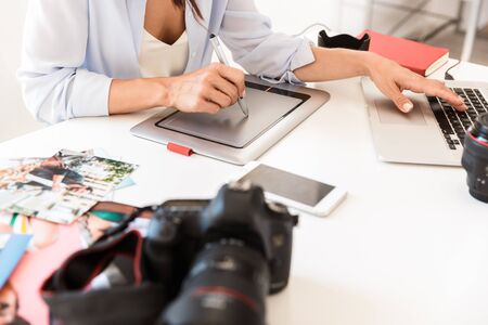 Close up of a young woman photographer working at her office while sitting at the desk, working with...