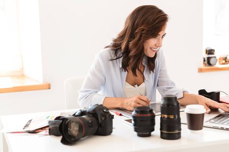 Beautiful young woman photographer working at her office while sitting at the desk, working with tablet for drawingの写真素材