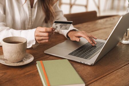 Cropped photo of young business woman sit indoors in office using laptop computer holding credit card.の写真素材
