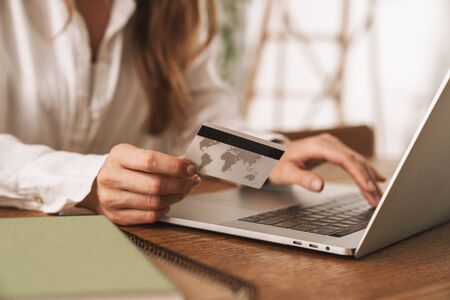 Cropped image of young business lady sit indoors in office using laptop computer holding credit...
