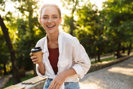 Close up of a smiling young girl walking at the city park, holding takeaway coffee
