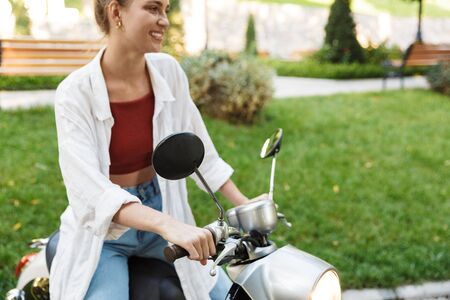 Cropped image pf a beautiful smiling young girl wearing casual summer clothing sitting on a scooter...