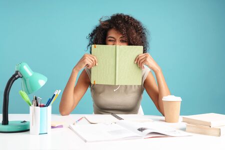 Beautiful young african businesswoman casually dressed sitting at the desk isolated over blue...